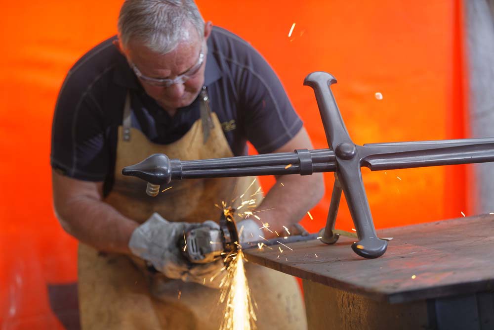 A CWGC blacksmith grinding metal while working on a Cross of Sacrifice.