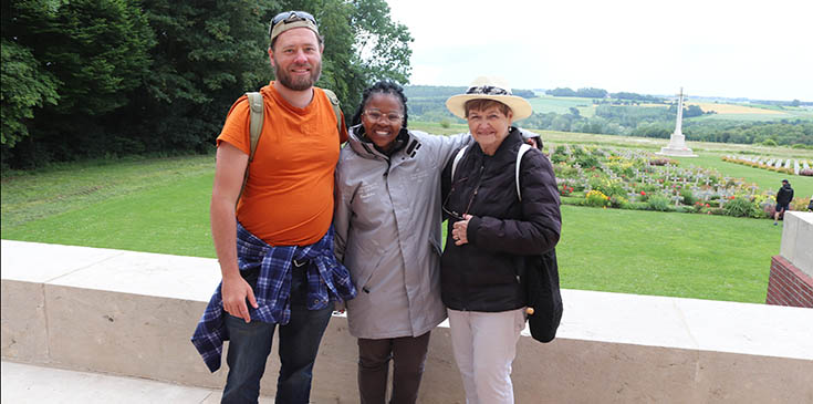 From left to right: Man in orange t shirt and jeans, black girl in a grey long coat, and a white woman in a straw hat and black coat.