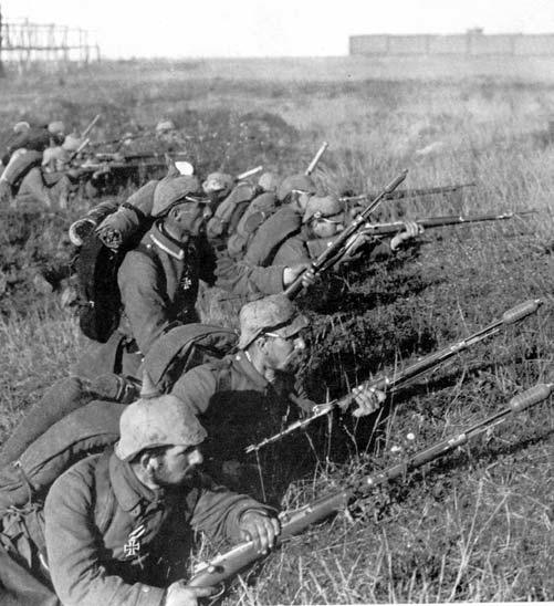 German troops wearing greatcoats and Pickelhaube helmets wait in a slip trench to attack during the Battle of the Marne. They are holding rifles equipped with bayonets.