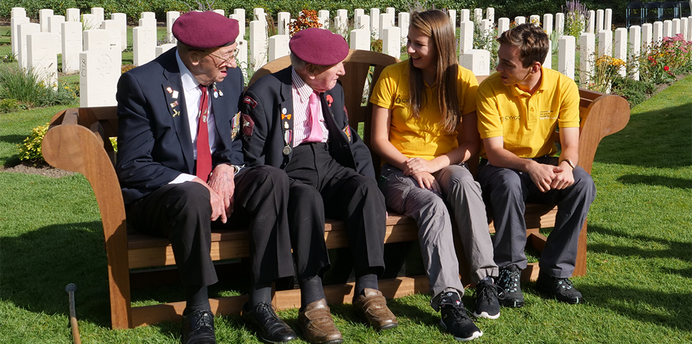 WW2 veterans and young CWGF guides chatting a bench in a CWGC cemetery.