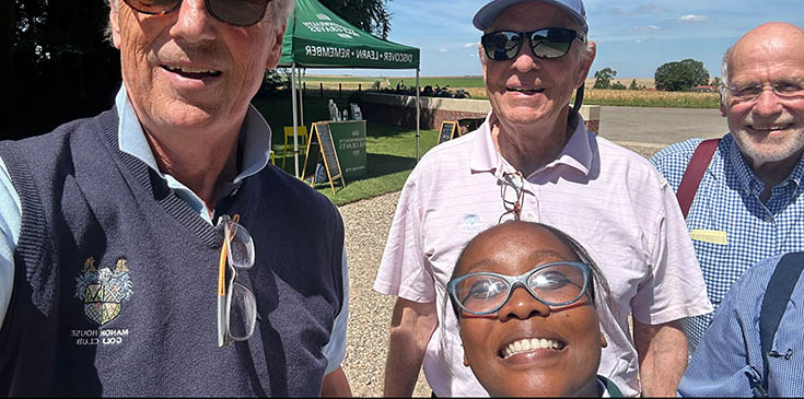 A group of elderly gentlmen pose for a photo with a young black soouth african woman outside the green CWGC marquee erected outside Thiepval.