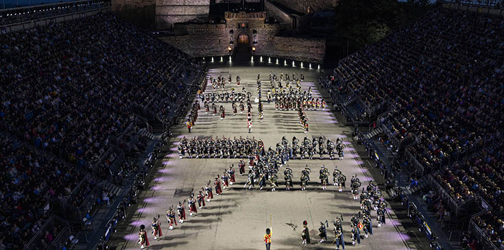 Edinburgh Military Tattoor facing Edinburgh Castle. Military figures are arrayed in formation during a parade. Two banks of stands flank the parade ground.