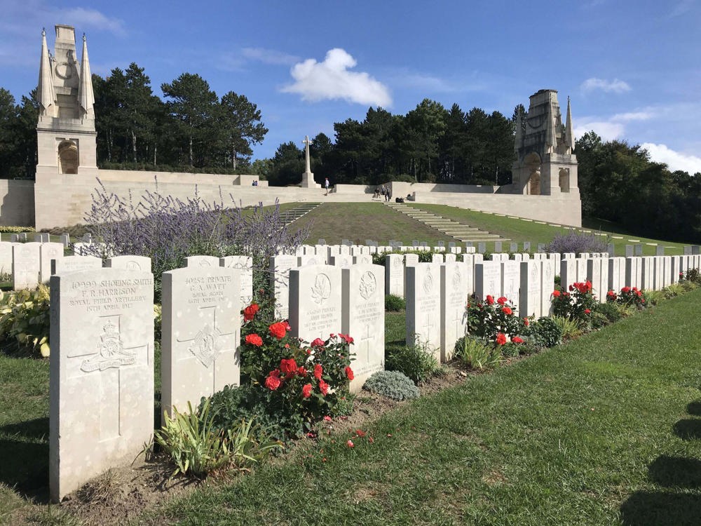 Row of headstones in front of the main central monument and cross of sacrifice at Etaples Military Cemetery.