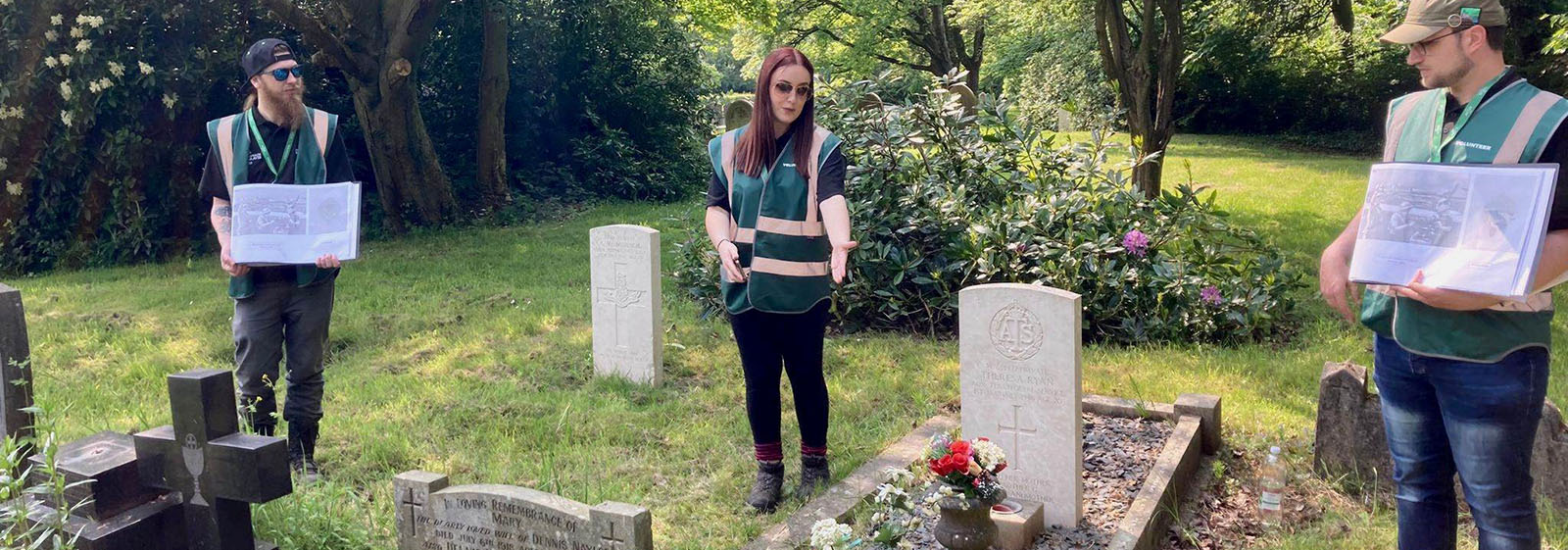 Three student volunteer tour guides giving a talk next to CWGC headstones.